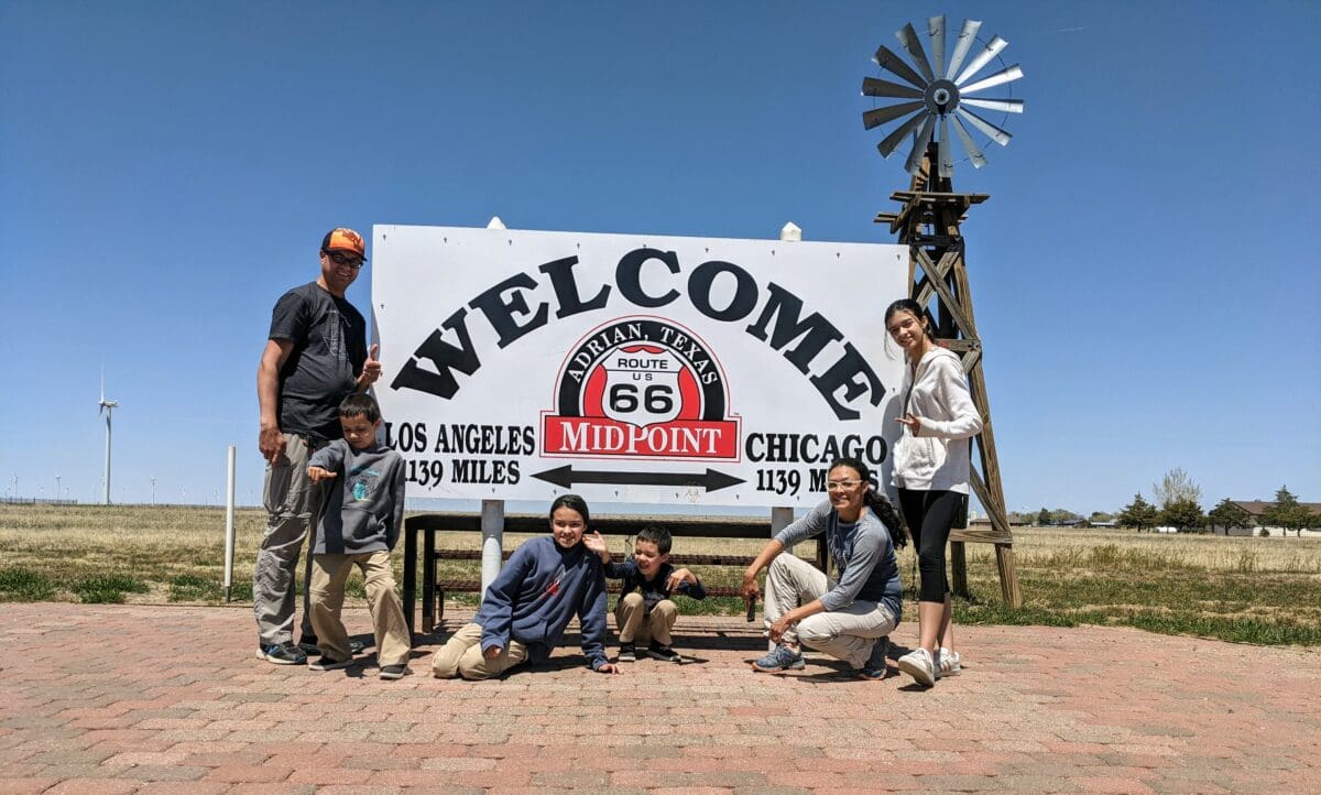 Family standing in front of a Welcome Midpoint Cafe sign on one of Route 66 must-see stops in Texas